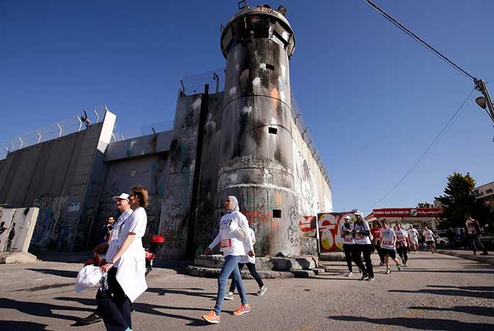 Participants in the Palestine Marathon in Bethlehem run by the 8 metre-high Separation Wall and one of its watch towers.