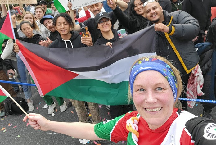 A woman running a marathon stops in front of a crowd waving Palestinian flags.