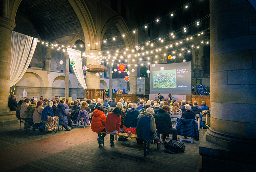 A congregation sit in an old church with a festoon of Christmas lights overhead.