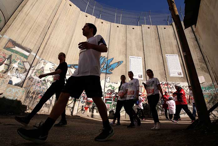 Marathon runners in Bethlehem walking alongside the illegal Separation Wall as part of the Palestine Marathon.