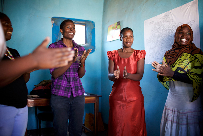 A group of young women from Tanzania singing and smiling together.