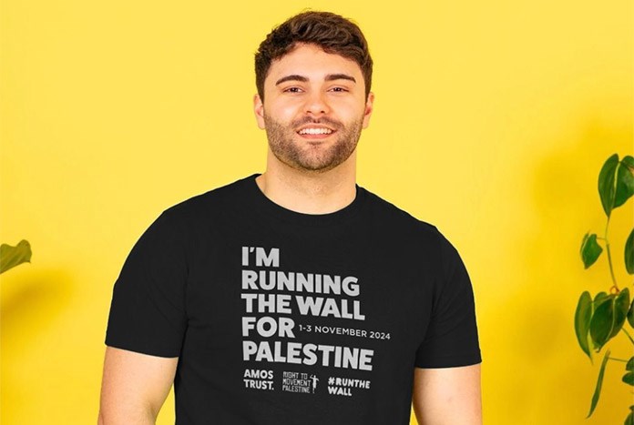 A man wears an Amos Trust I'm Running The Wall for Palestine black T-shirt