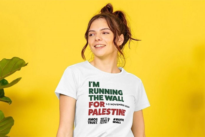 A young woman wears an Amos Trust I'm Running The Wall for Palestine white T-shirt