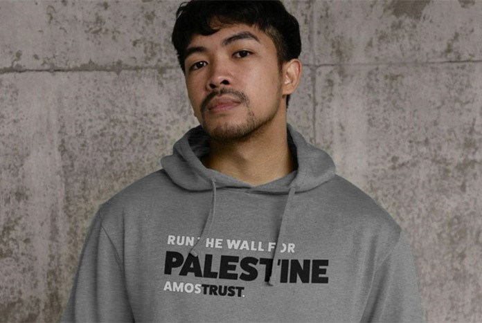 A young man wears an Amos Trust 'Run The Wall for Palestine' grey hoodie.