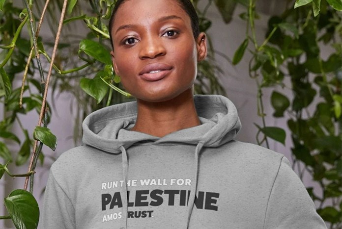 A young woman wears an Amos Trust Run The Wall for Palestine grey hoodie.