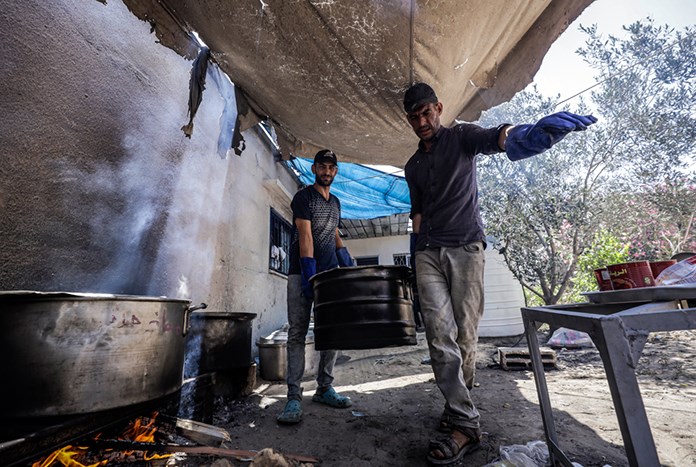 Two men carry a large cooking pot in Gaza.