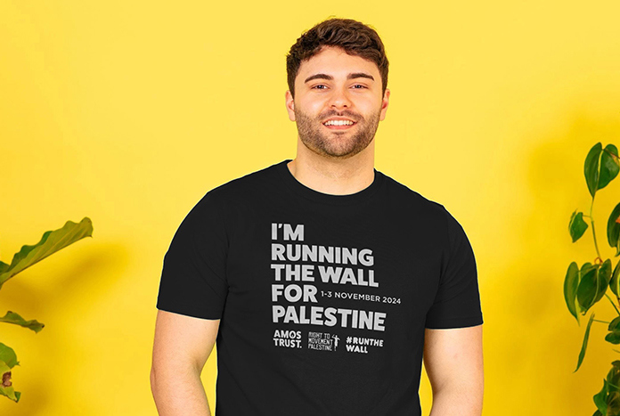 A young man wears a black Amos Trust "I'm Running The Wall For Palestine' T-shirt.