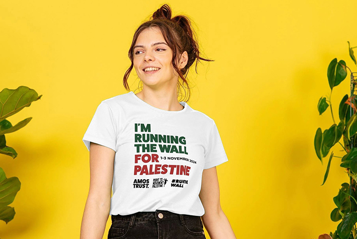 A young woman wears a white Amos Trust "I'm Running The Wall For Palestine' T-shirt.