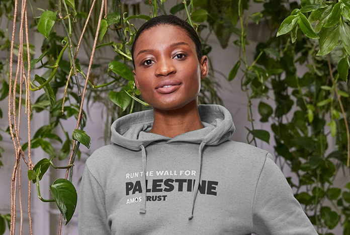 A young woman wears a grey Amos Trust "I'm Running The Wall For Palestine' Hoodie.