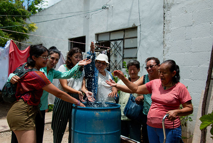 A group of female climate activists in Mexico pouring water into a water barrel.