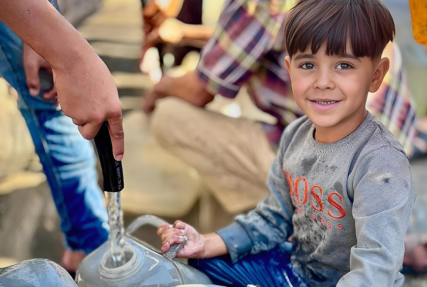 A young boy smiles as he collects water in Gaza