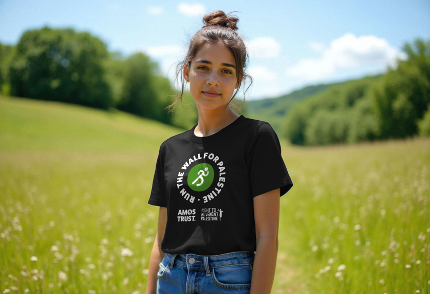 A young woman wearing a black Amos Trust 'Run The Wall for Palestine' T-shirt in a meadow.